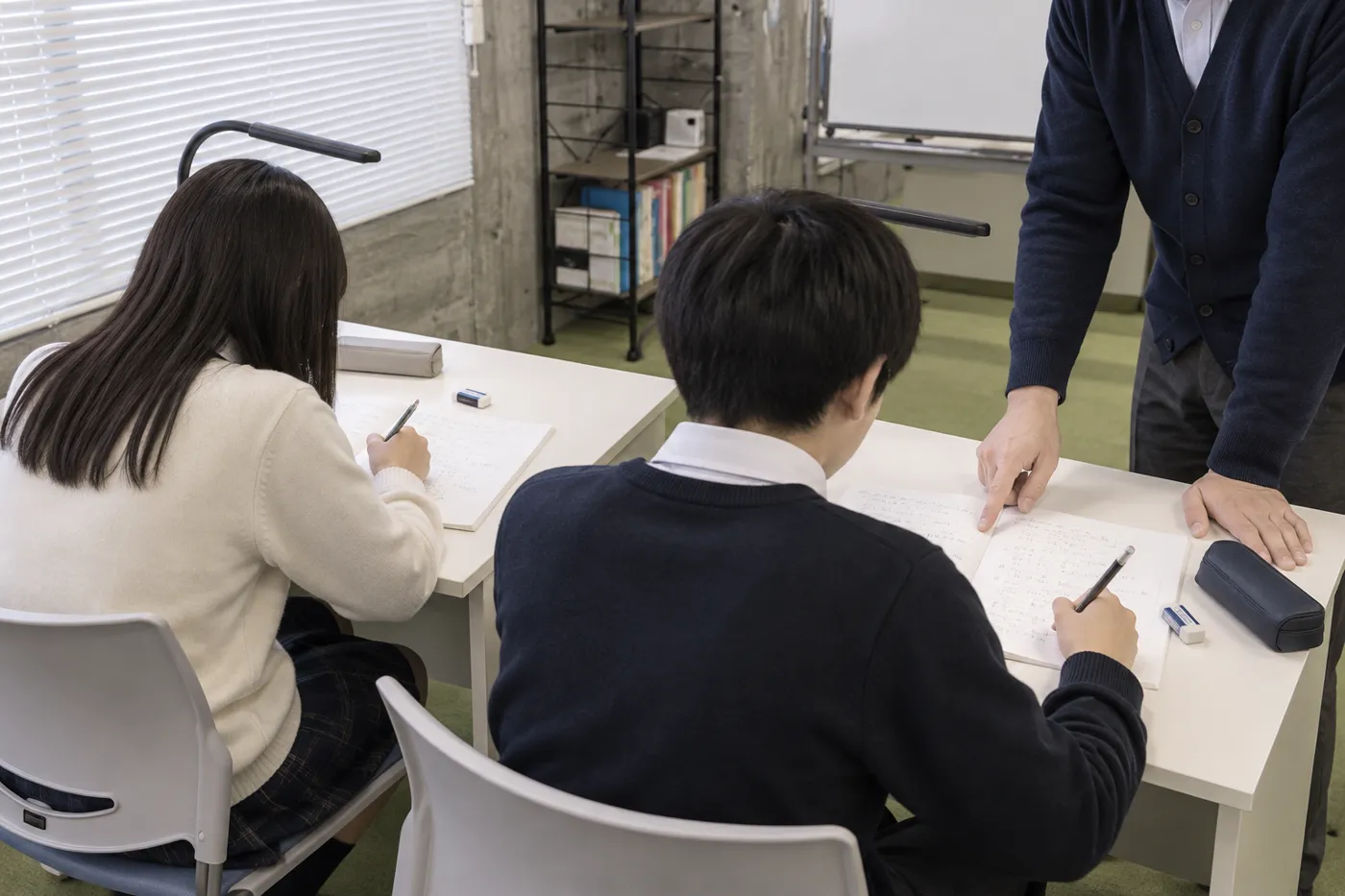 講師1人が生徒2人のノートを見ている授業の様子